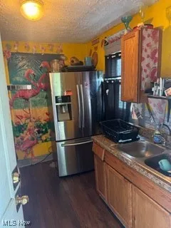 Kitchen featuring a textured ceiling, stainless steel refrigerator with ice dispenser, brown cabinetry, and dark wood-type flooring