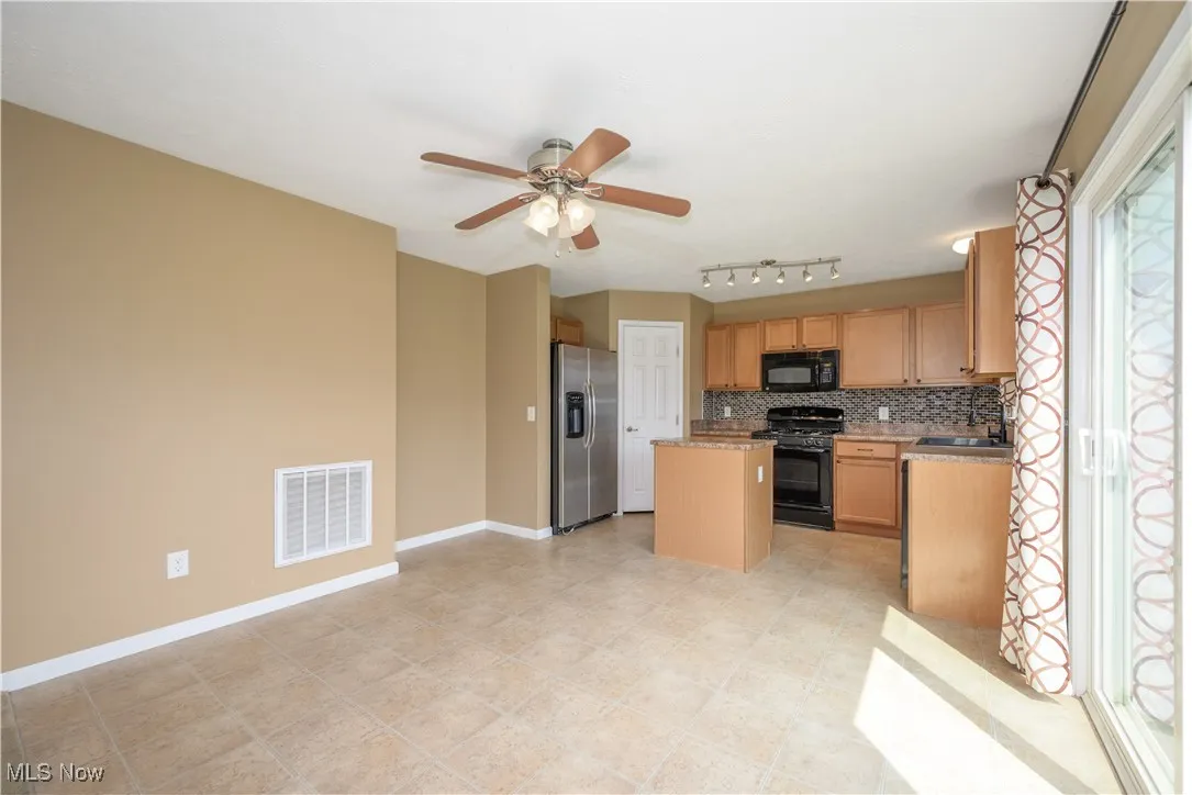 Kitchen with a kitchen island, tasteful backsplash, black appliances, light countertops, and ceiling fan