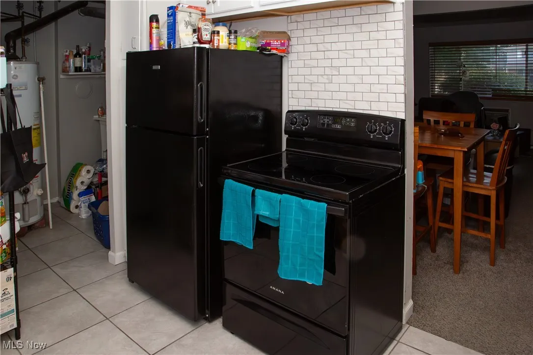 Kitchen featuring black appliances, light tile patterned floors, water heater, white cabinets, and backsplash