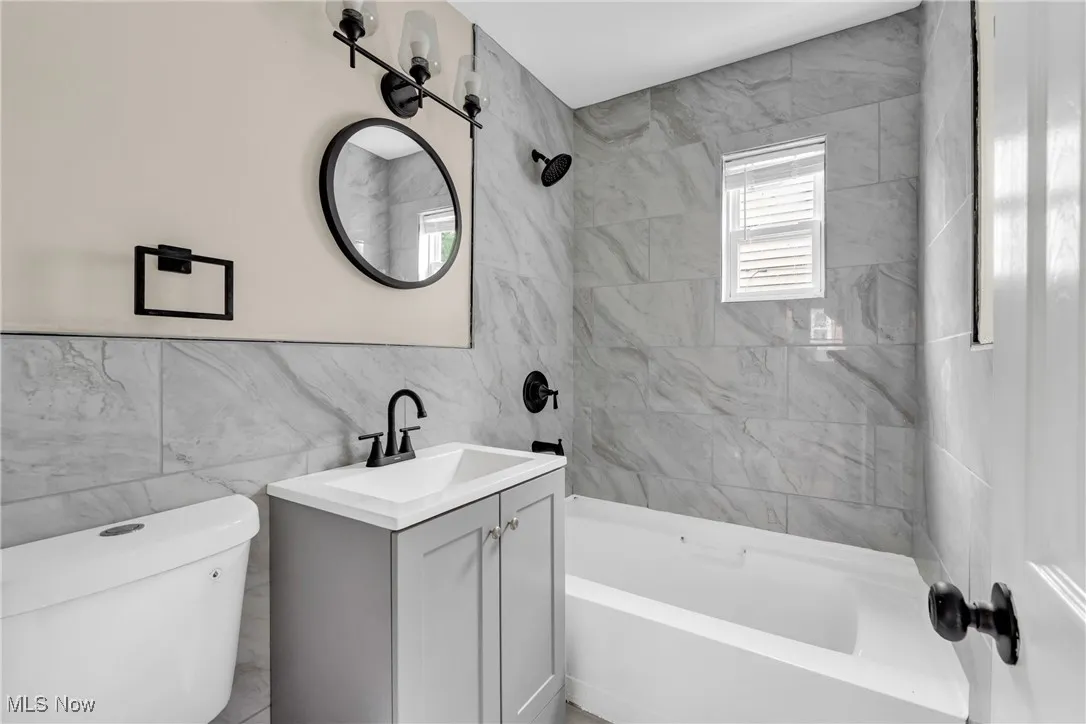Full bath with tile walls, vanity, and tub / shower combination