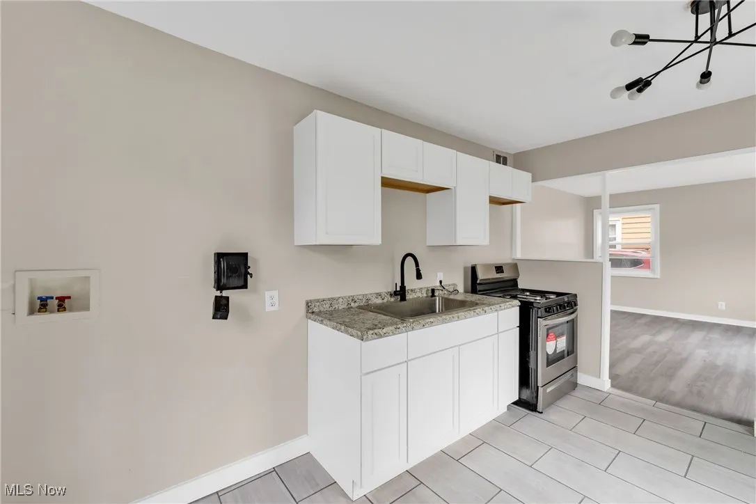 Kitchen with stainless steel range oven, white cabinetry, light countertops, light wood-type flooring, and a chandelier