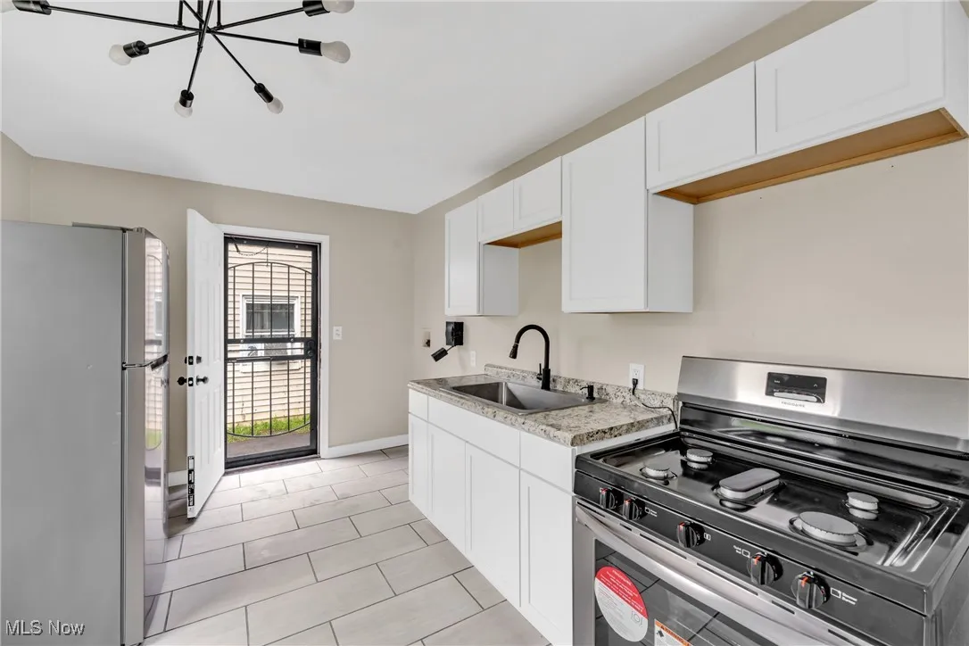 Kitchen with gas stove, freestanding refrigerator, white cabinetry, a chandelier, and light tile patterned floors