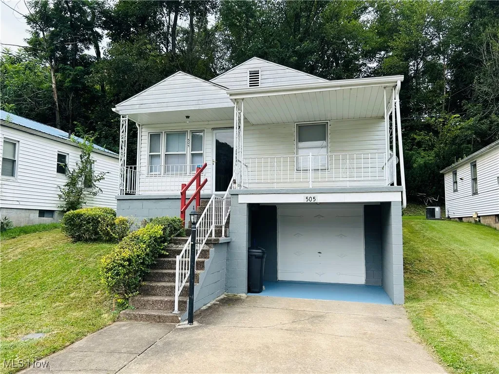 Front view of front of home with driveway, an attached garage, a front yard, stairs, and covered porch