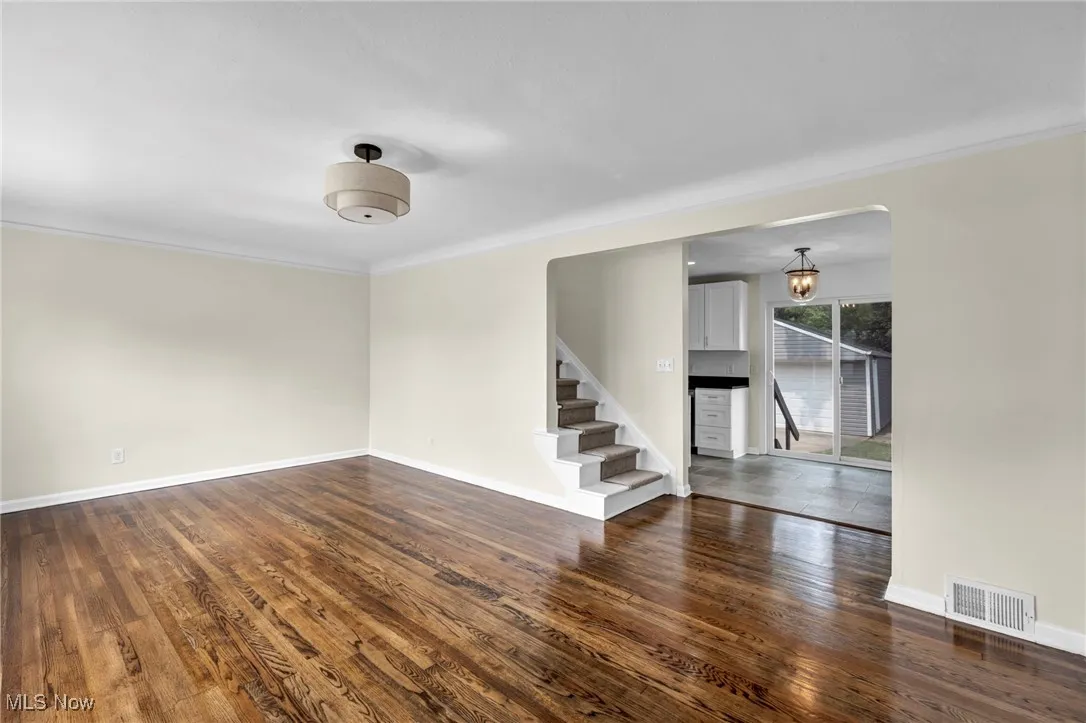 Unfurnished living room featuring stairs, dark wood-type flooring, crown molding, and arched walkways