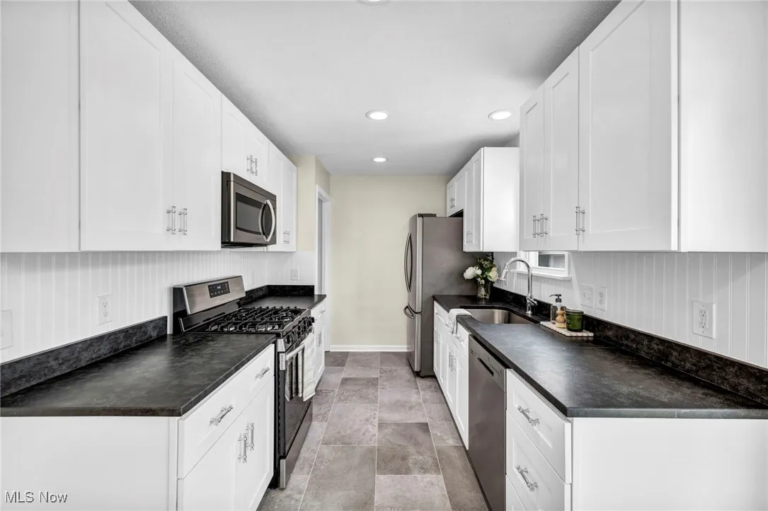Kitchen featuring stainless steel appliances, dark countertops, white cabinetry, and recessed lighting