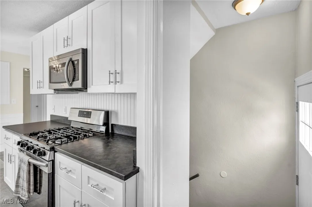 Kitchen featuring stainless steel appliances, dark countertops, white cabinetry, and a textured ceiling
