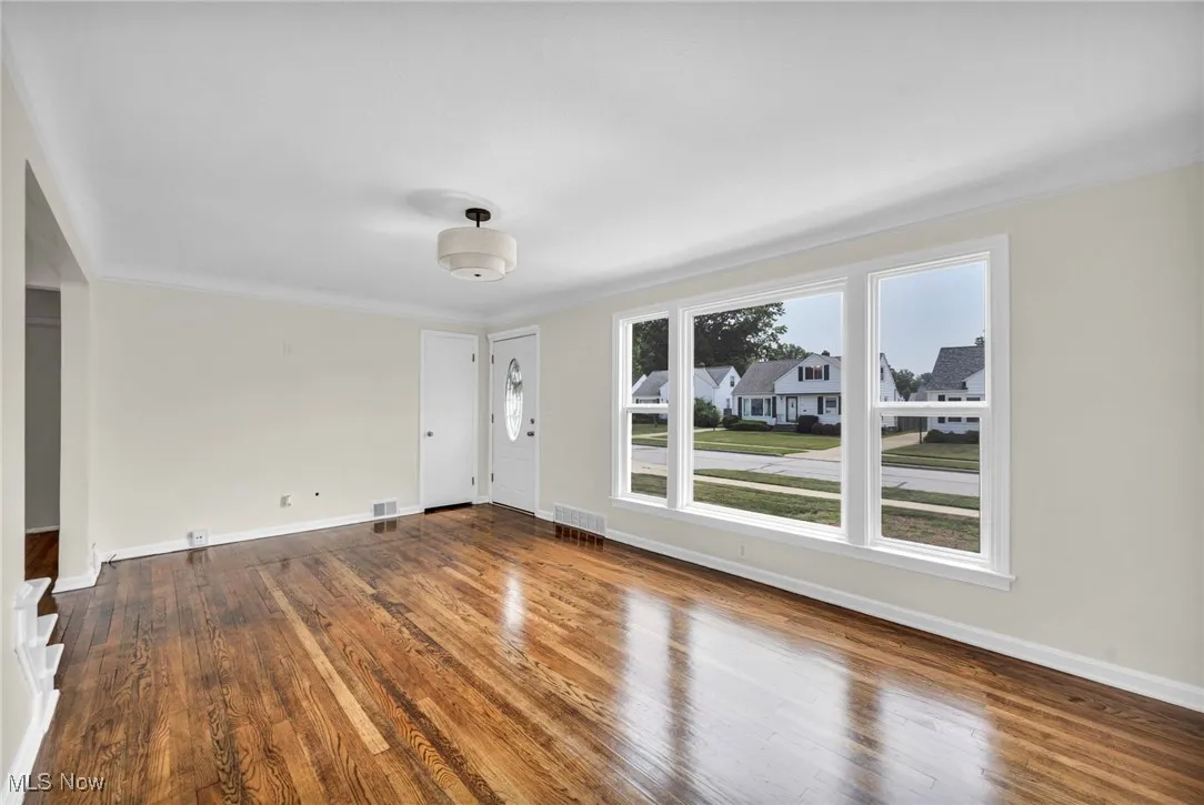 Unfurnished living room with wood finished floors, crown molding, and a residential view