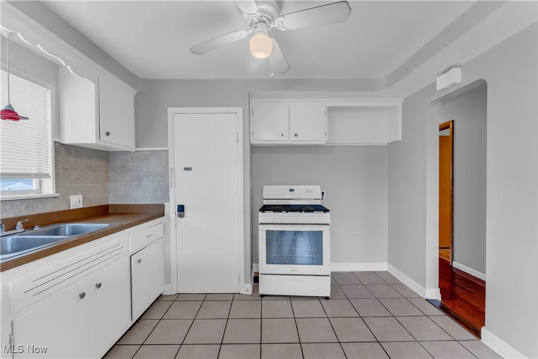 Kitchen featuring white range with gas stovetop, light tile patterned flooring, a ceiling fan, white cabinets, and dark countertops