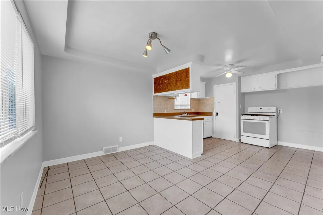 Kitchen with white gas stove, a peninsula, light tile patterned floors, white cabinetry, and backsplash