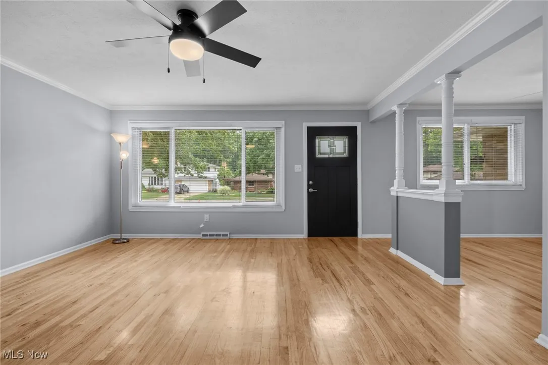 Entrance foyer with crown molding, light wood finished floors, a ceiling fan, and decorative columns