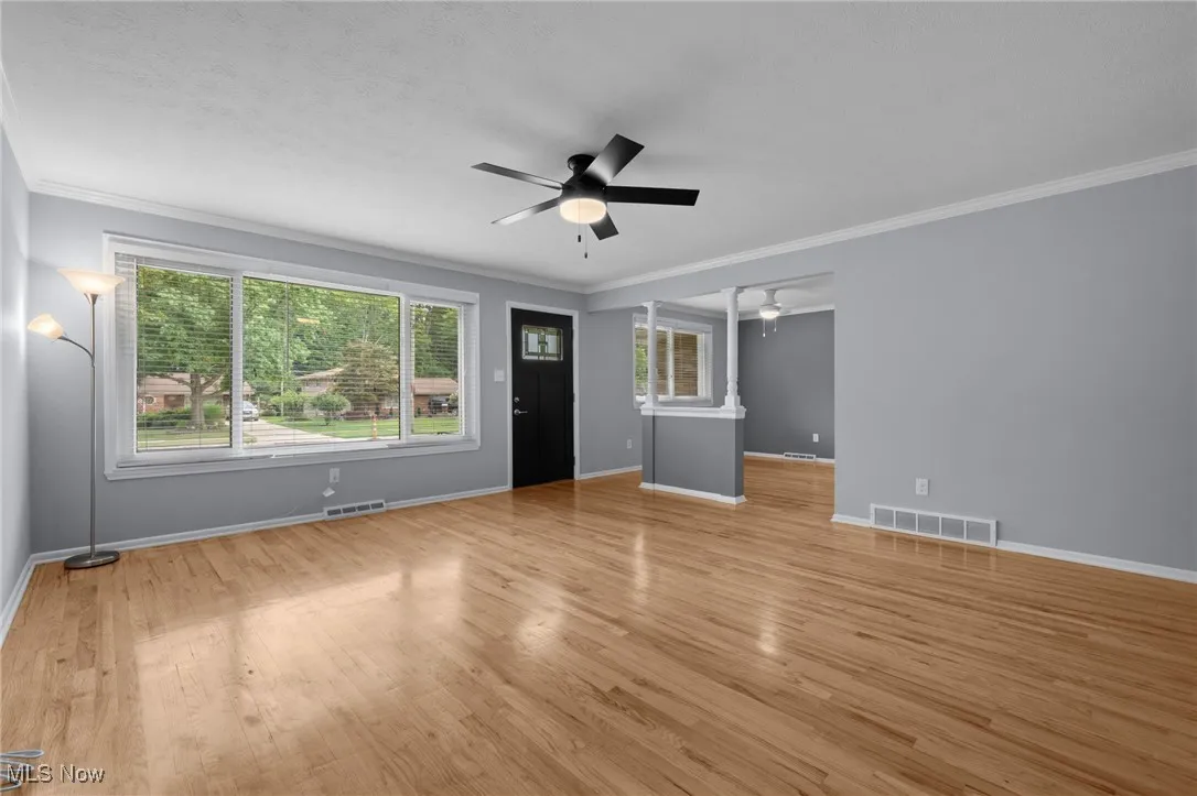 Unfurnished living room featuring ornamental molding, light wood-type flooring, and a ceiling fan
