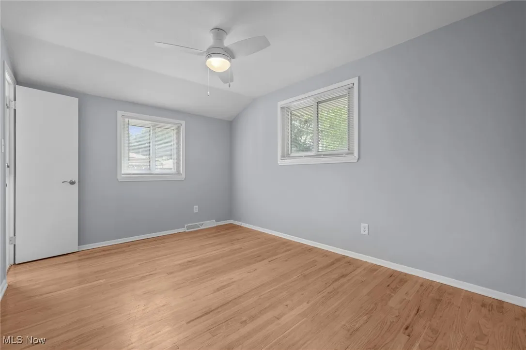 Spare room with plenty of natural light, light wood finished floors, vaulted ceiling, and a ceiling fan