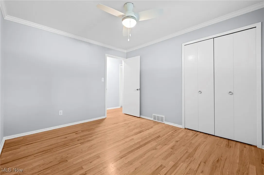 Unfurnished bedroom with crown molding, wood finished floors, a closet, and a ceiling fan
