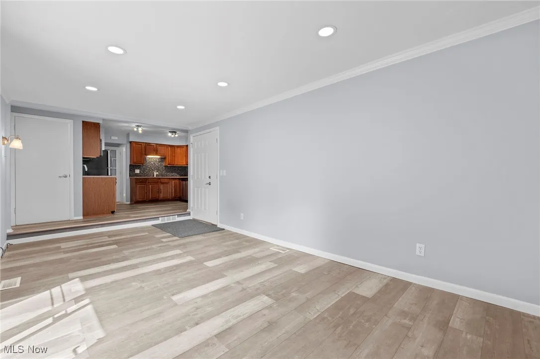 Unfurnished living room featuring light wood-type flooring, ornamental molding, and recessed lighting