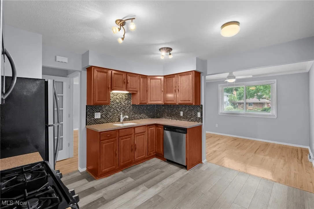 Kitchen featuring light countertops, light wood finished floors, decorative backsplash, appliances with stainless steel finishes, and brown cabinets