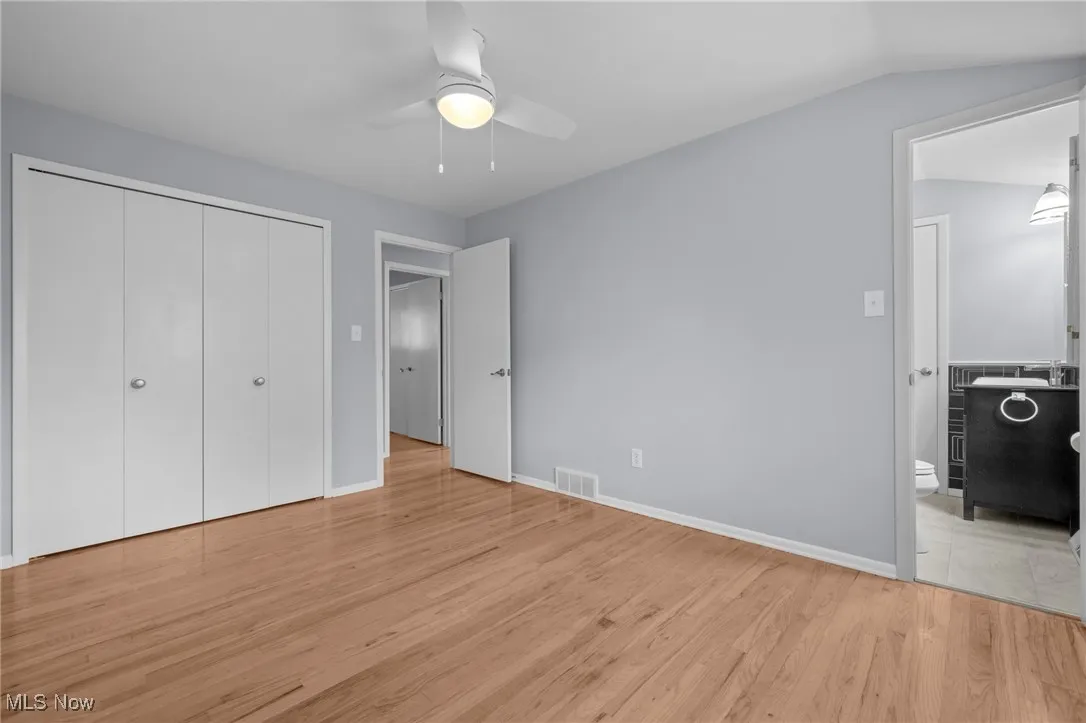 Unfurnished bedroom featuring light wood-type flooring, a closet, ensuite bathroom, and ceiling fan