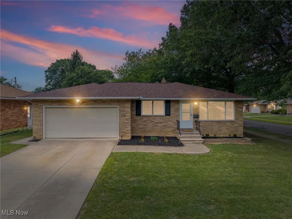 Ranch-style home with brick siding, roof with shingles, a lawn, and concrete driveway