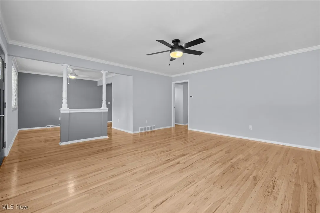 Unfurnished living room featuring ceiling fan, crown molding, and light wood-type flooring