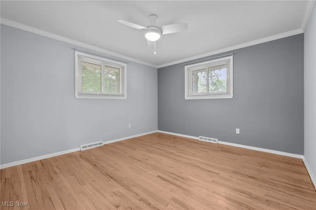 Spare room featuring light wood-style floors, crown molding, and ceiling fan