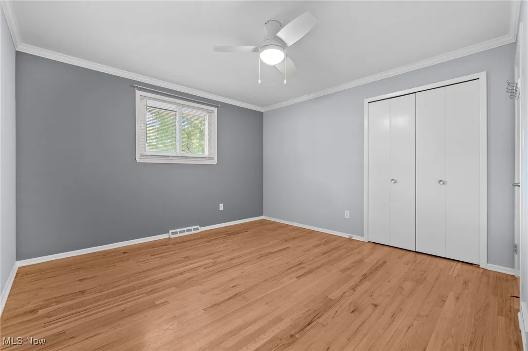 Unfurnished bedroom featuring ornamental molding, light wood-style flooring, a closet, and ceiling fan