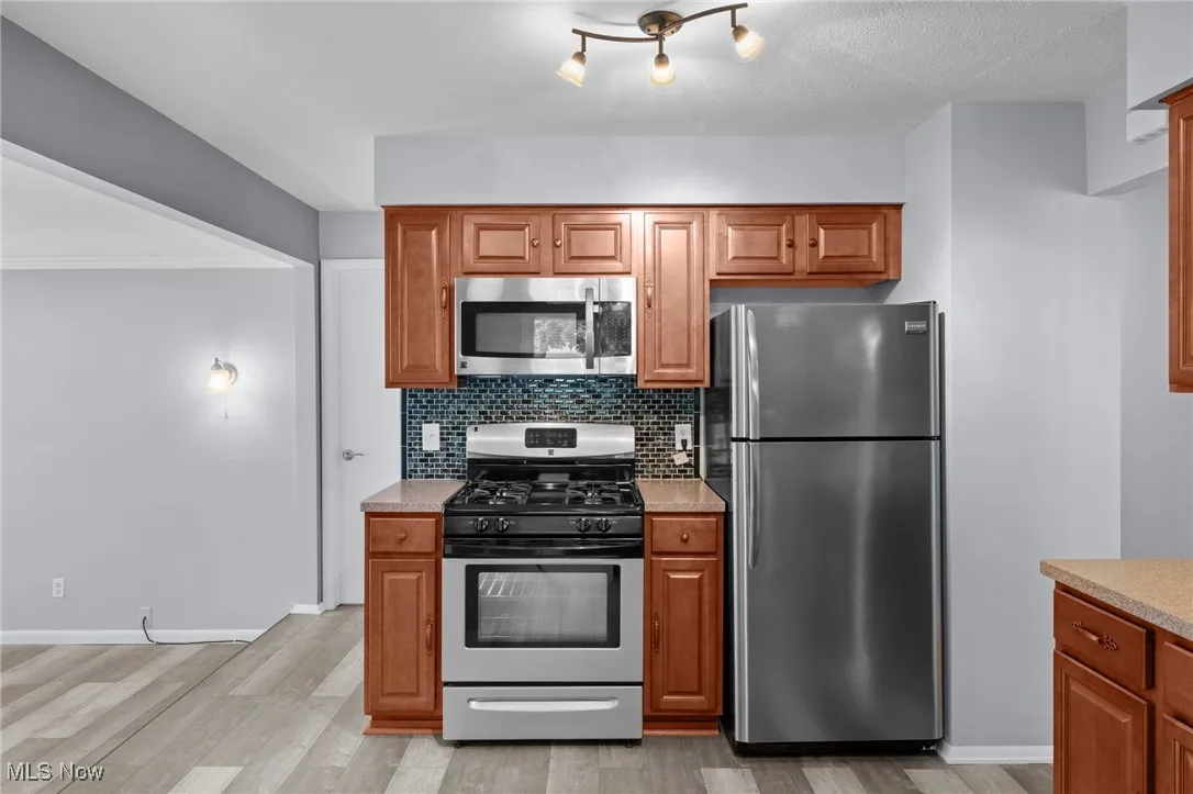Kitchen featuring stainless steel appliances, light countertops, light wood-style floors, tasteful backsplash, and brown cabinetry