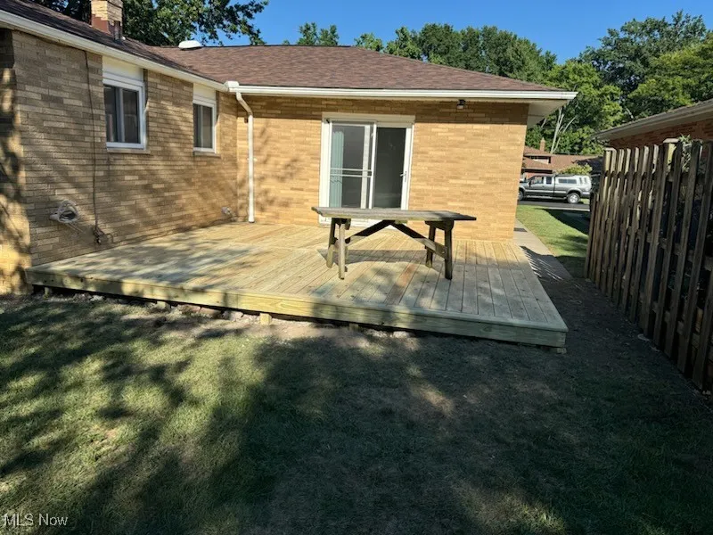 Back of house featuring a wooden deck, brick siding, a chimney, and a lawn