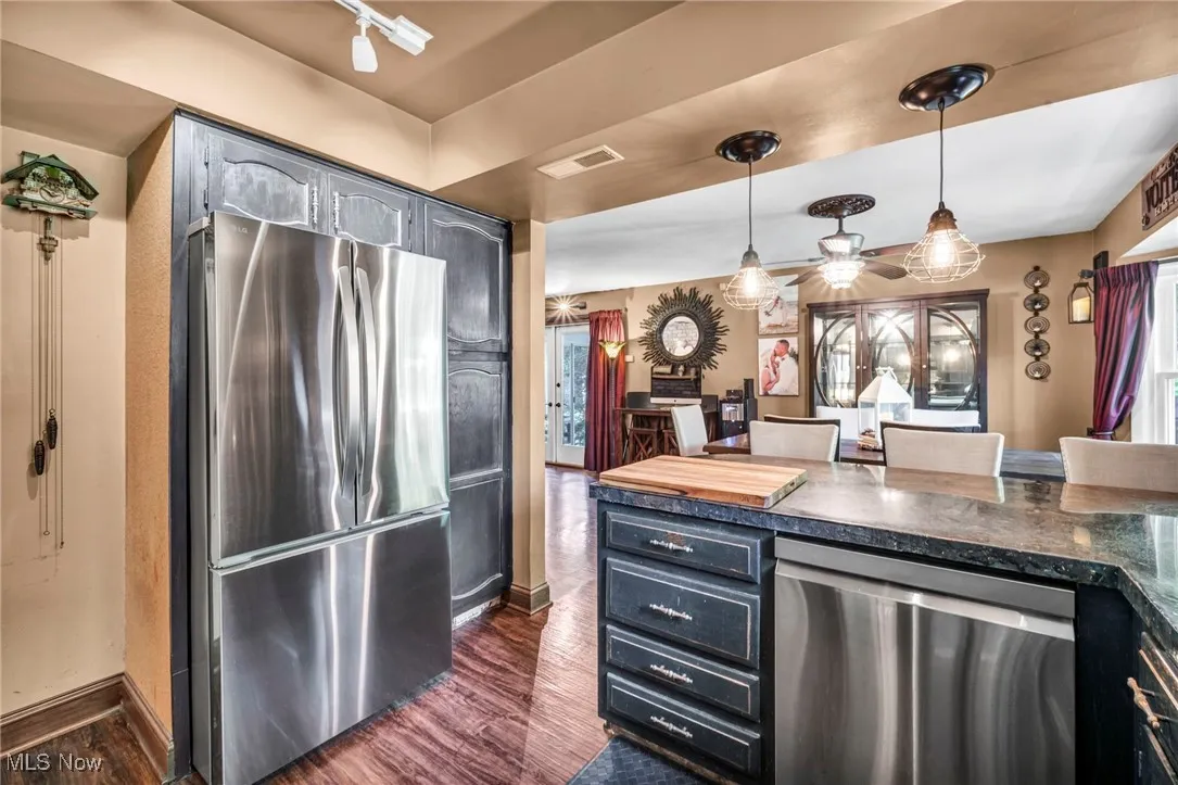 Kitchen featuring appliances with stainless steel finishes, dark wood finished floors, dark countertops, and hanging light fixtures
