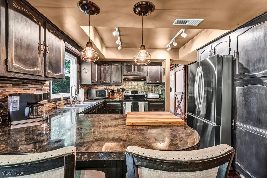 Kitchen featuring dark countertops, track lighting, stainless steel appliances, and a peninsula