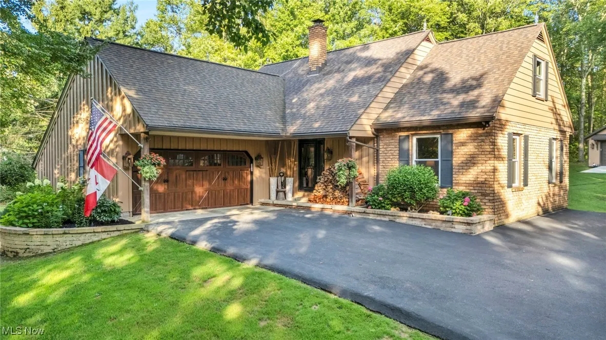 View of front of house with brick siding, asphalt driveway, a shingled roof, a chimney, and a garage