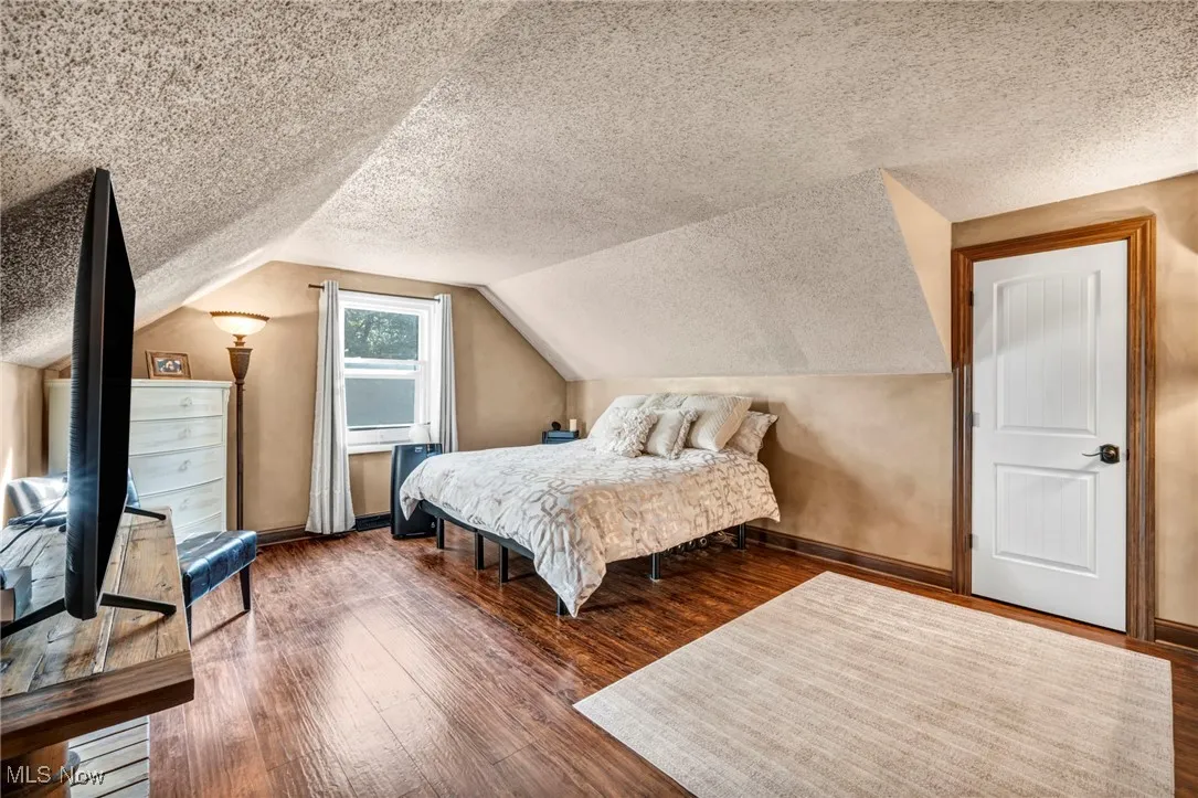 Bedroom with a textured ceiling, wood finished floors, and lofted ceiling