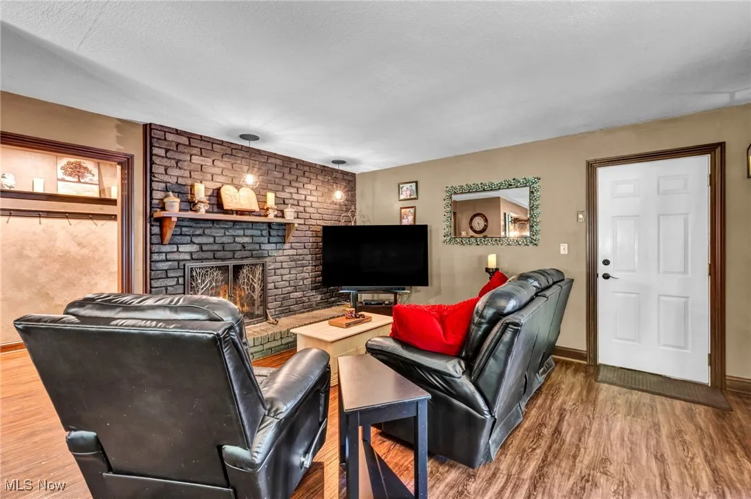 Living room with a brick fireplace, wood finished floors, and a textured ceiling