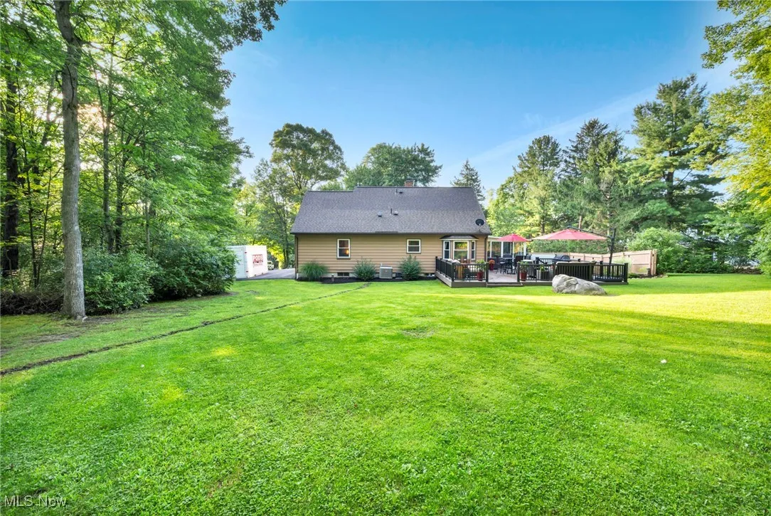 Rear view of house with a deck, a lawn, and view of wooded area