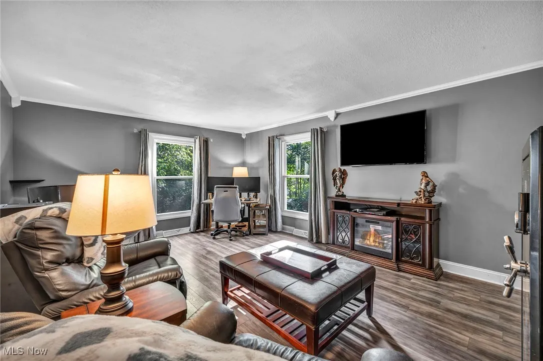 Living area with ornamental molding, wood finished floors, an office area, a glass covered fireplace, and a textured ceiling