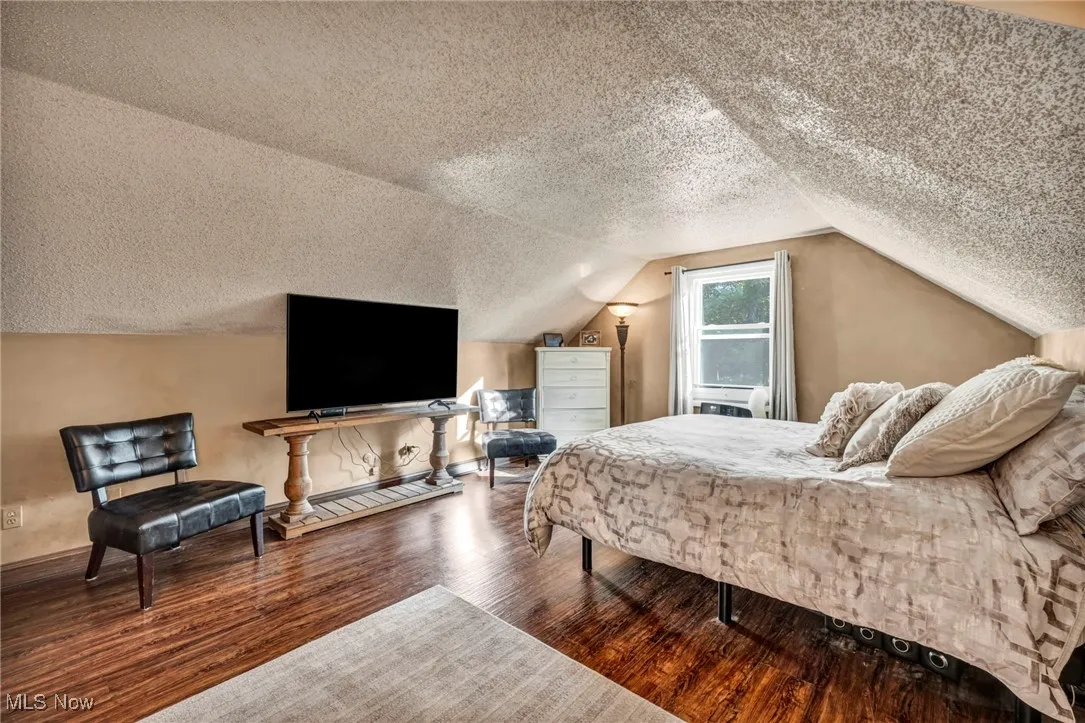 Bedroom featuring a textured ceiling, wood finished floors, and vaulted ceiling