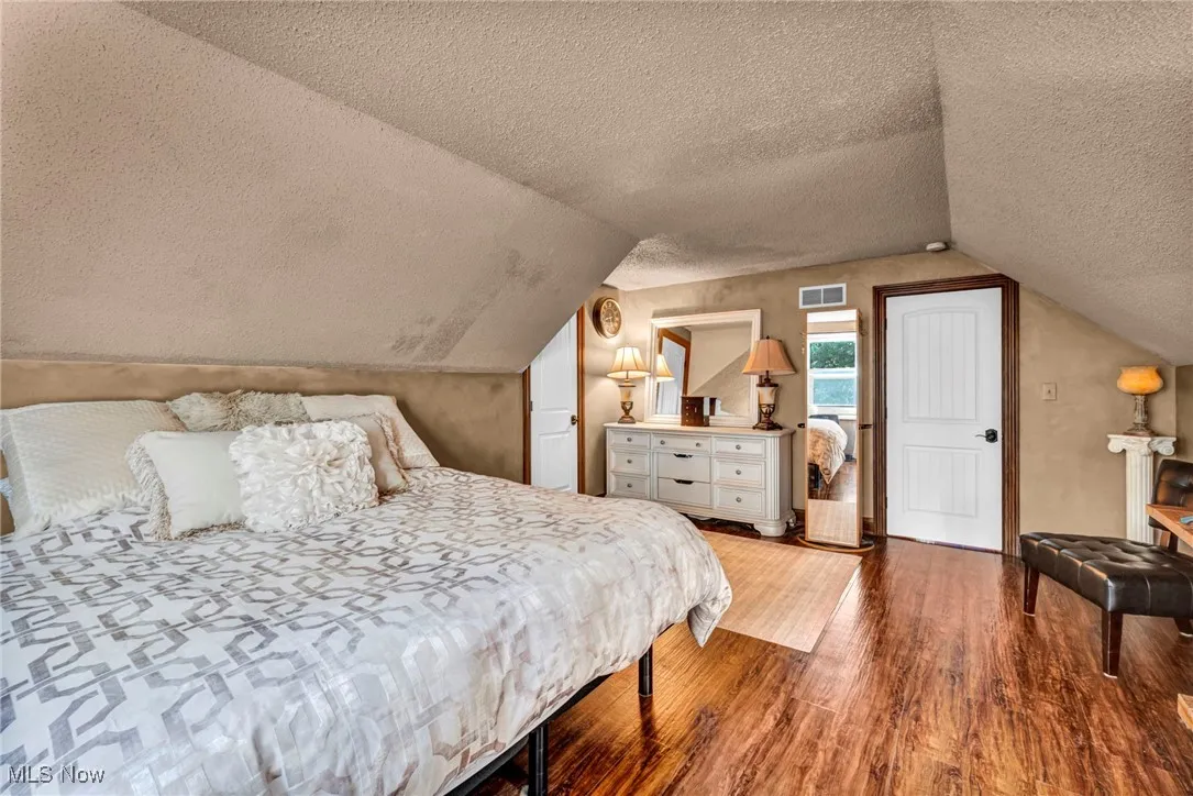 Bedroom with wood finished floors, a textured ceiling, and lofted ceiling