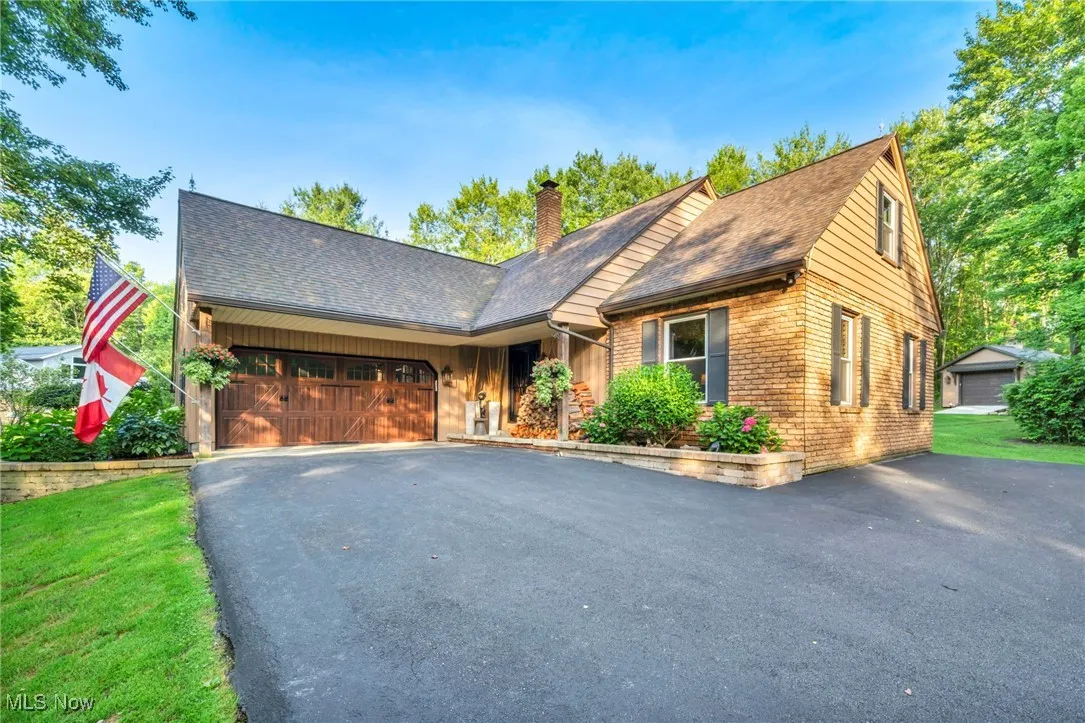 View of front of house featuring brick siding, driveway, a chimney, a shingled roof, and an attached garage