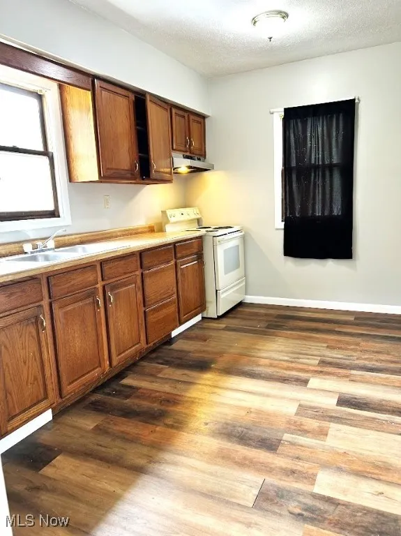 Kitchen featuring white electric stove, brown cabinets, a textured ceiling, and wood finished floors
