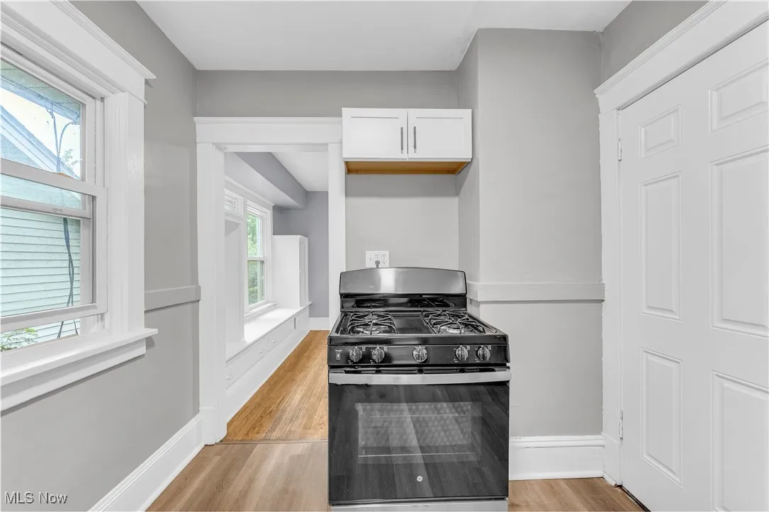 Kitchen with black range with gas stovetop, light wood-type flooring, and white cabinets