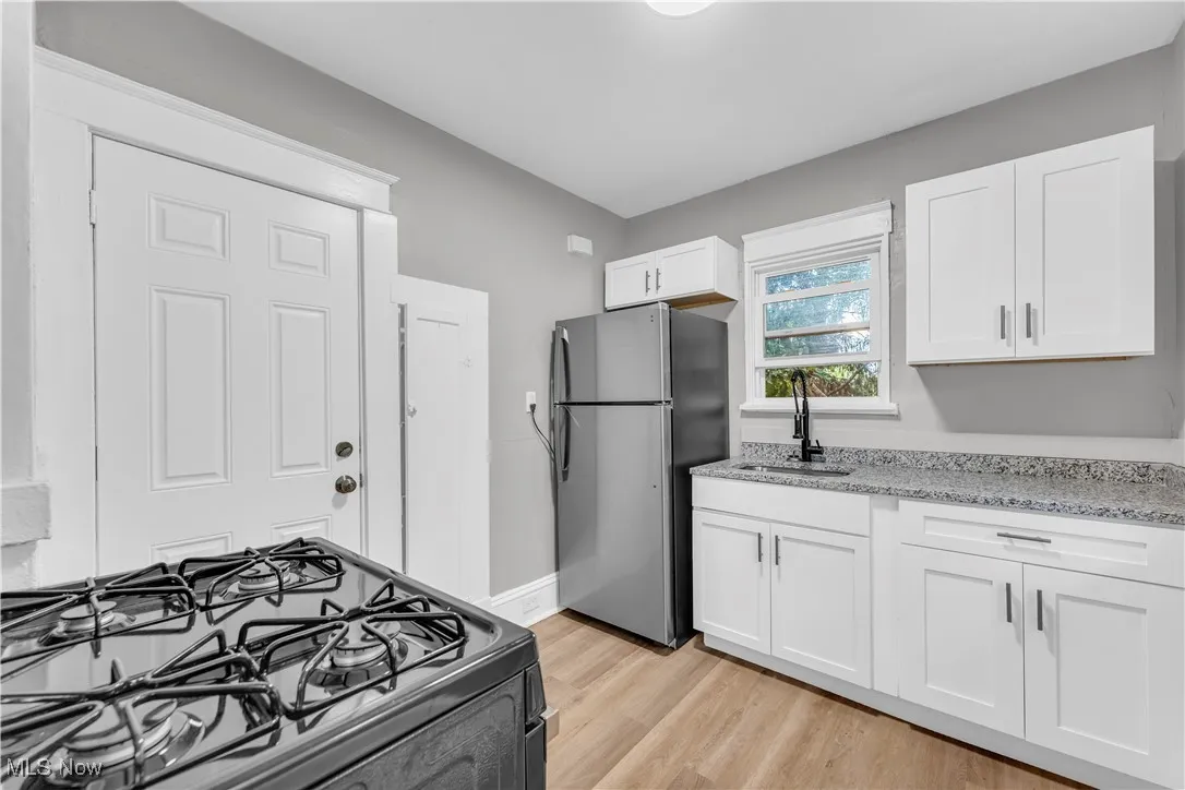 Kitchen with black gas range oven, light wood-type flooring, freestanding refrigerator, white cabinets, and light stone counters