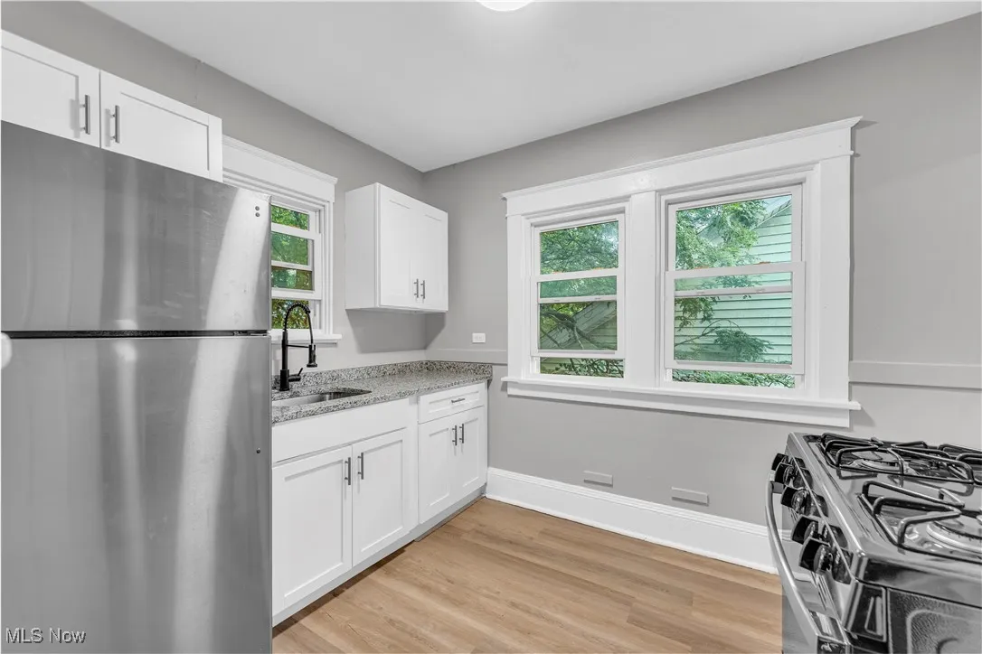 Kitchen with appliances with stainless steel finishes, light wood finished floors, white cabinets, and light stone counters