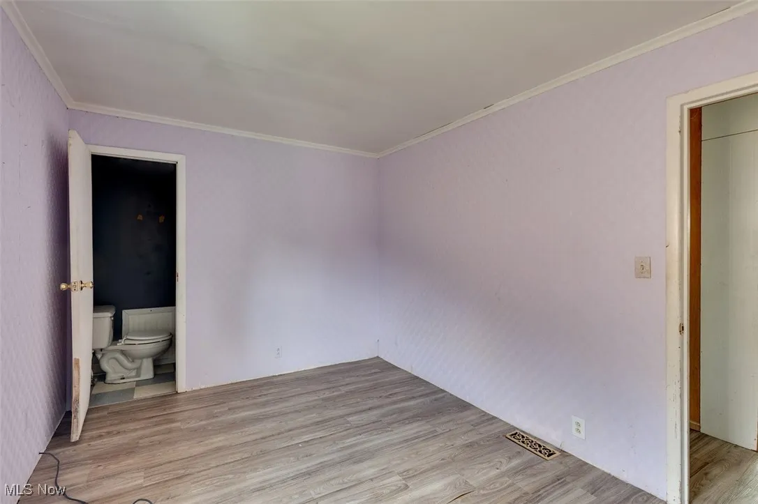 Unfurnished bedroom with wood finished floors, ornamental molding, and ensuite bath