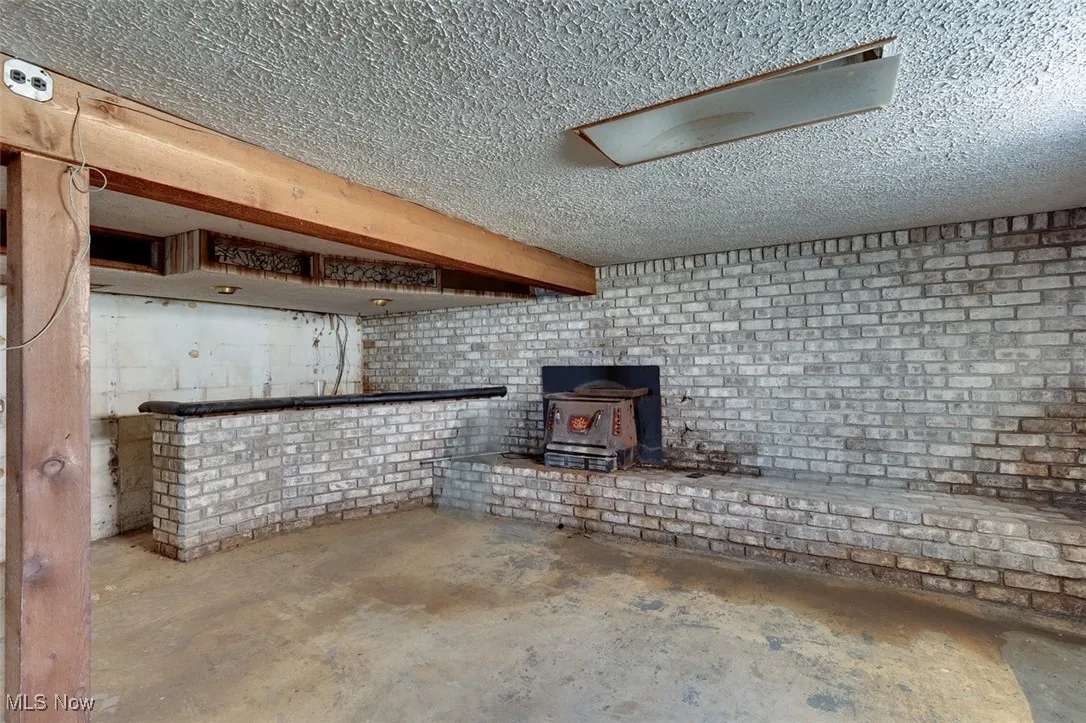 Below grade area with a wood stove, brick wall, and a textured ceiling