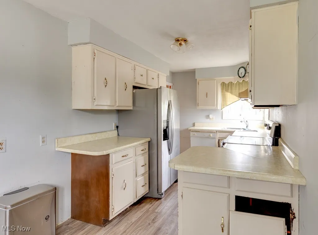 Kitchen with light countertops, stove, light wood-style flooring, and stainless steel fridge with ice dispenser
