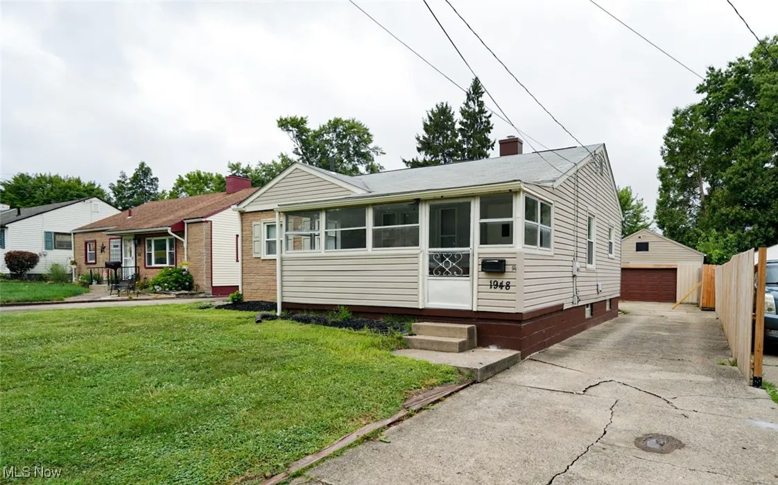 View of front of home with an outbuilding, a front lawn, a detached garage, a chimney, and a sunroom