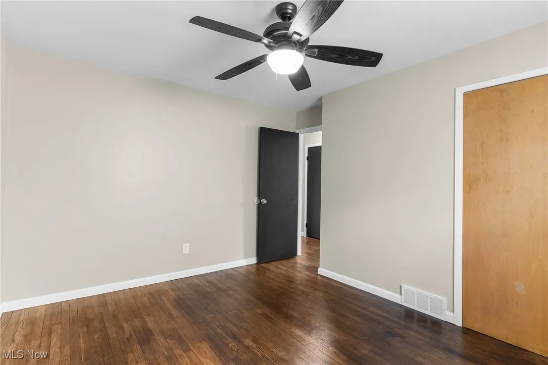 Unfurnished room featuring dark wood-type flooring, baseboards, visible vents, and a ceiling fan