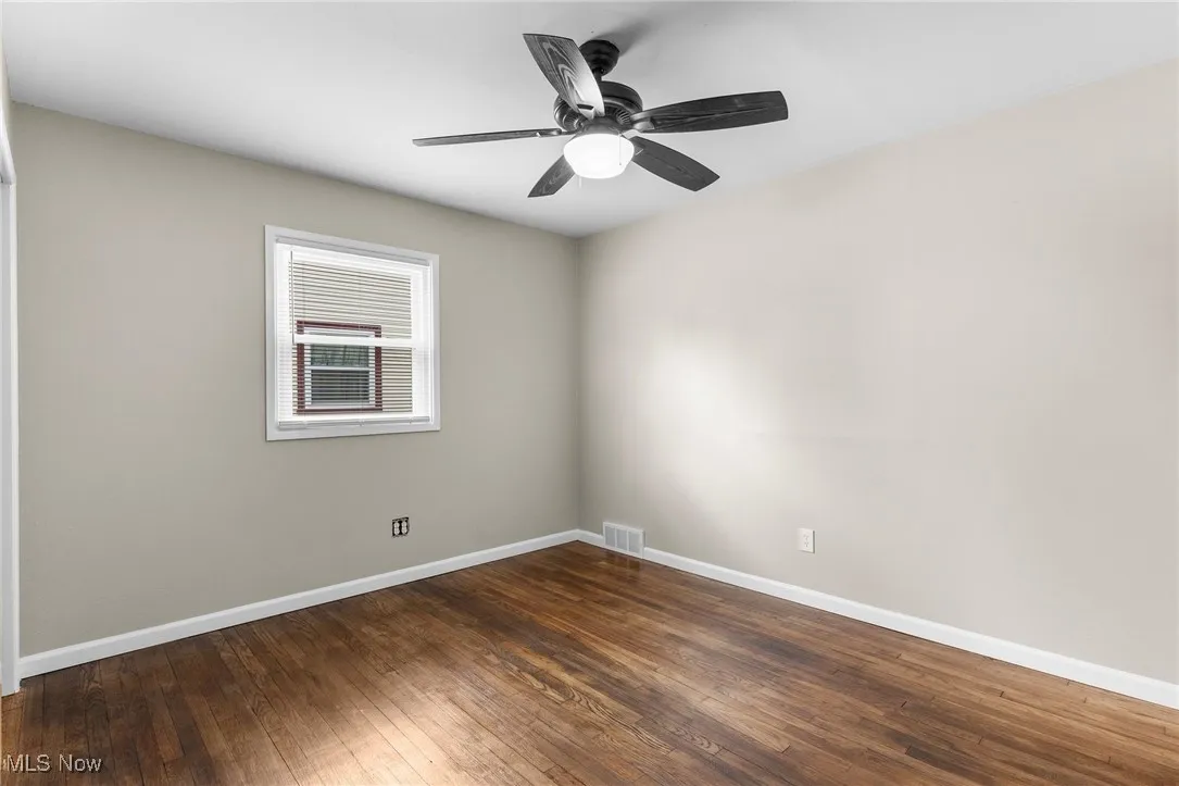 Spare room with dark wood-style floors, visible vents, ceiling fan, and baseboards