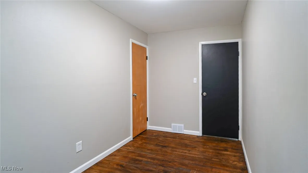 Empty room with dark wood-type flooring and baseboards