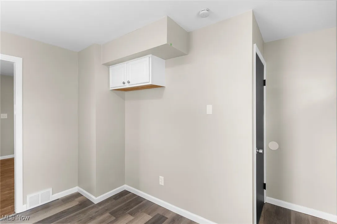 Laundry area featuring dark wood finished floors, baseboards, and visible vents