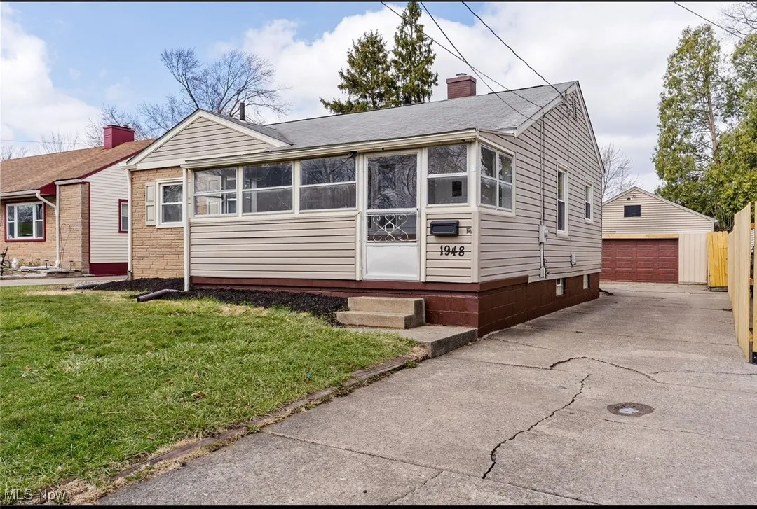 View of front of house with an outbuilding, a chimney, a garage, a front lawn, and a sunroom