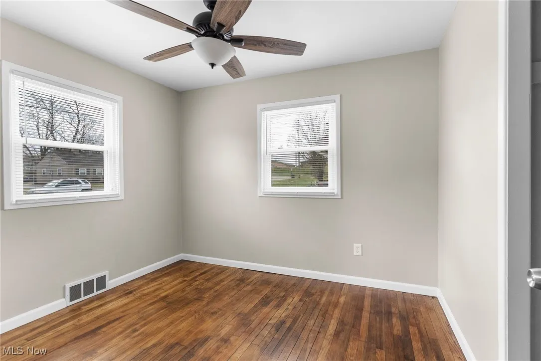 Unfurnished room featuring a ceiling fan, hardwood / wood-style flooring, baseboards, and visible vents